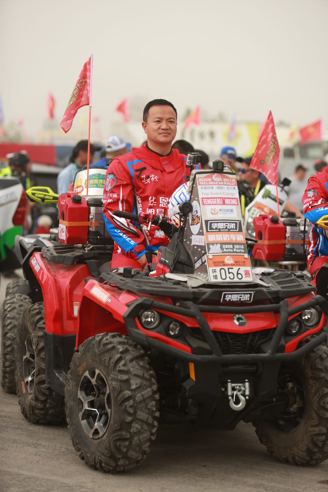 2019年环塔拉力赛发车现场,李铁军身穿赛车服站在四轮摩托车旁。
