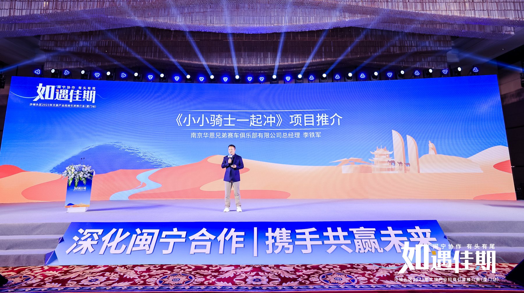 李铁军站在大型蓝色舞台屏幕前演讲，屏幕显示小小骑士一起冲项目推介。